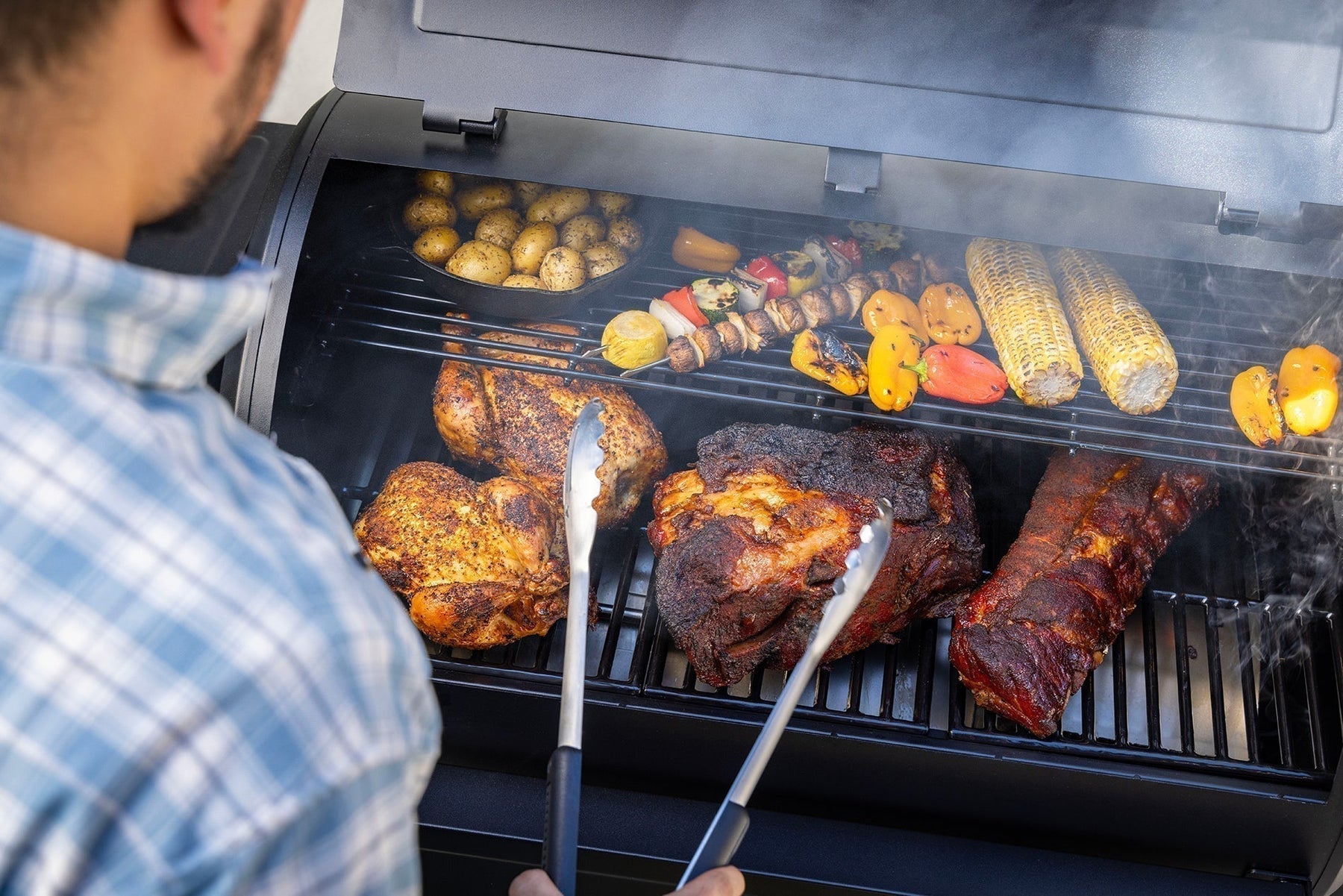 Man grilling meats and veggies with tongs on Pit Boss wood pellet grill