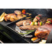 Black grill with steaks, vegetables, and skewers cooking.