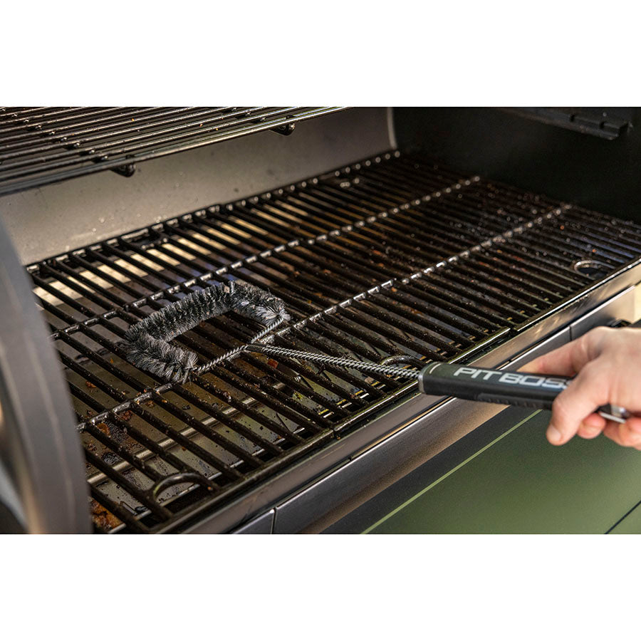 Black grill brush cleaning a black grill with "PIT605" handle.