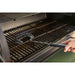Black grill brush cleaning a black grill with "PIT605" handle.