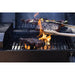 Close-up of steaks and skewered vegetables grilling over open flames on a barbecue grill, with tongs holding one steak.