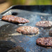 Grilled burger patties cooking on a flat-top griddle.