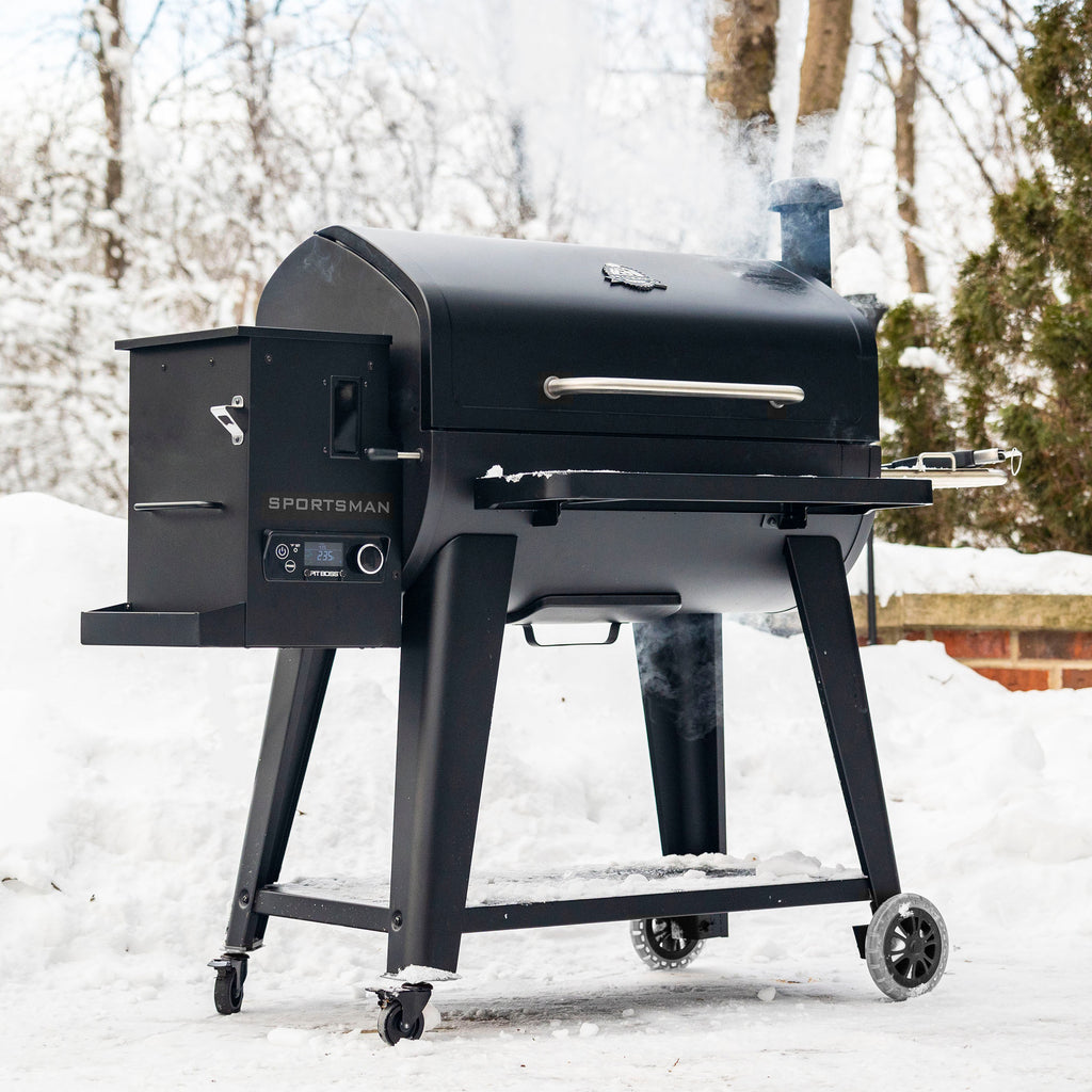 Black Sportsman pellet grill with digital control panel, smoking in snowy outdoor setting.