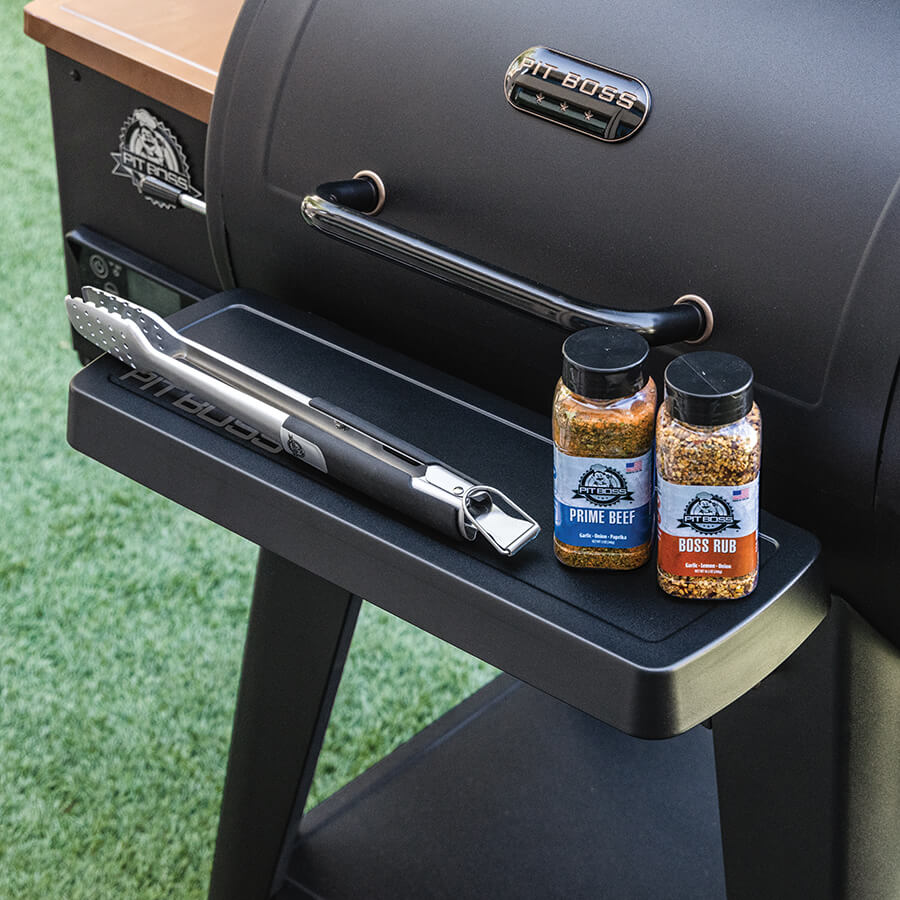 Black Pit Boss grill with seasoning bottles and tongs on side shelf.