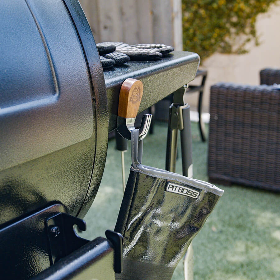 Green Pit Boss grill with wooden tool holder and black gloves on top.