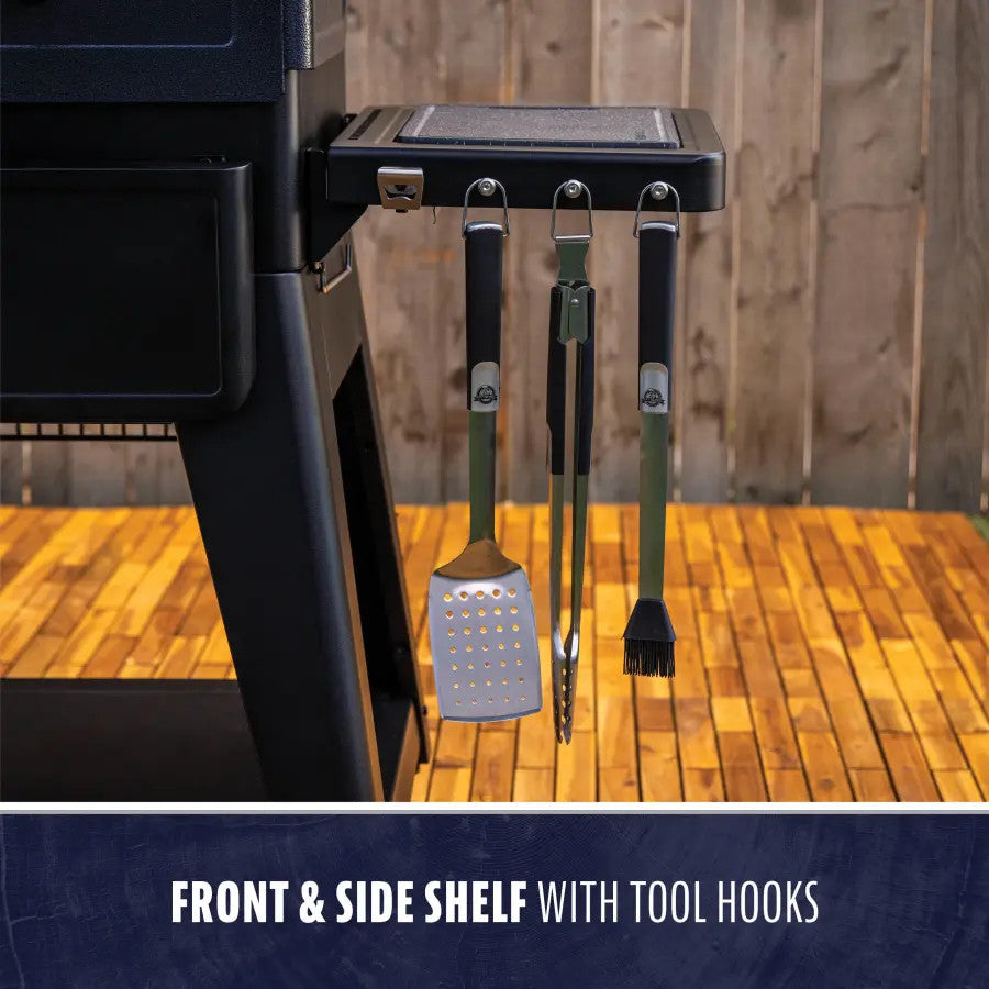 Black grill with front and side shelf, tool hooks holding spatula, tongs, and brush.
