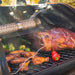 Black electric grill with smoking tube, cooking meat, chicken, and vegetables.