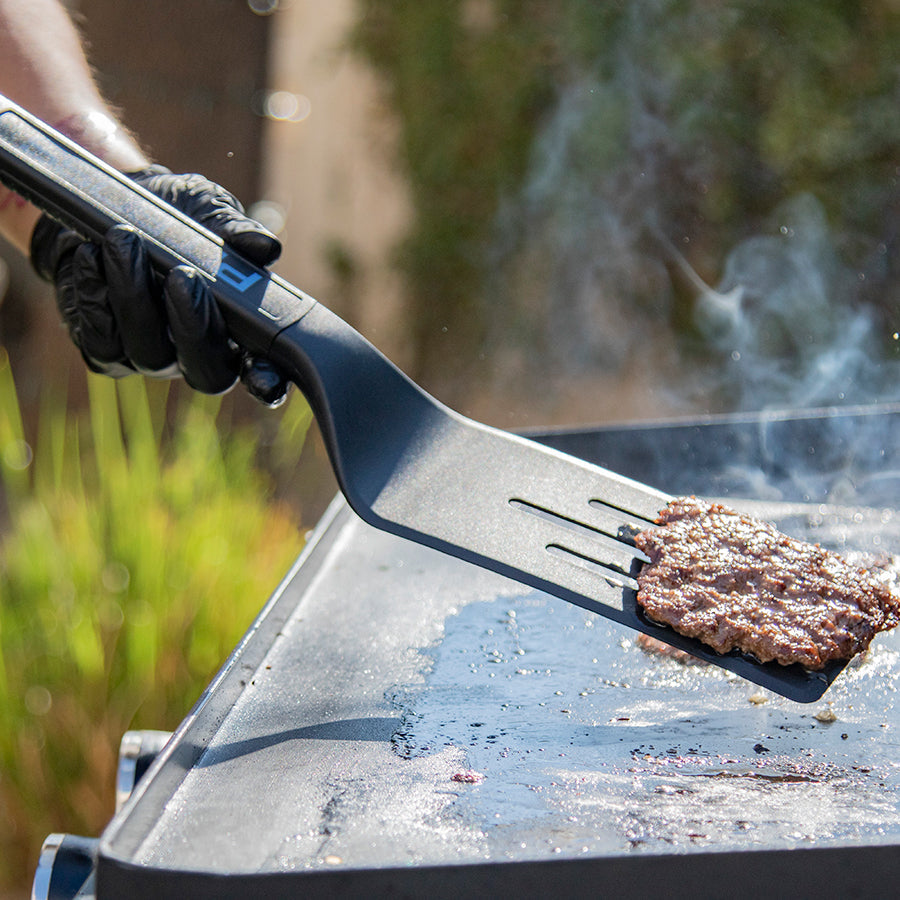 Black spatula flipping burger on grill.
