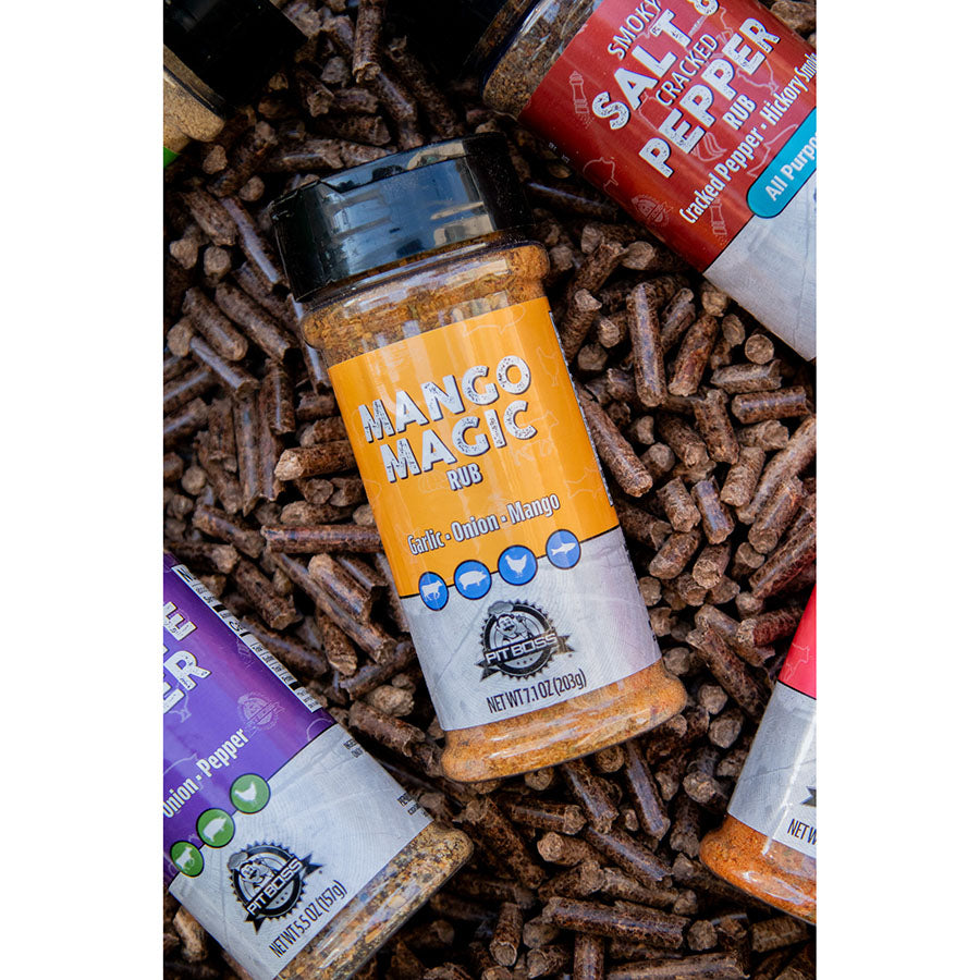 Pit Boss Mango Magic BBQ Rub Spice Bottle, Yellow and White laying in hardwood pellets