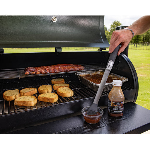 lifestyle_1, Silver tongs with black handle and small pit boss logo. Pictured dipped into texas mesquite bbq sauce