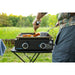 Front view of man using his portable griddle on a camping table making breakfast in the forest.
