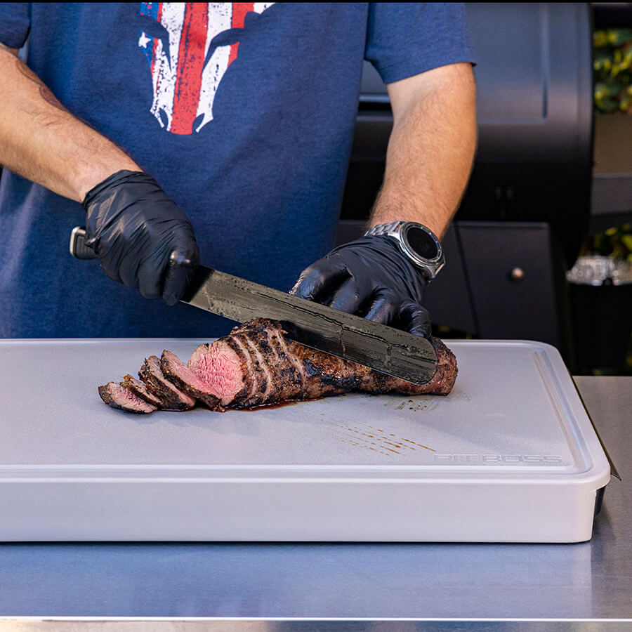 White cutting board with black gloves slicing cooked meat.