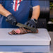 White cutting board with black gloves slicing cooked meat.