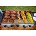 Silver flat-top grill cooking steaks, onions, vegetables, and asparagus.