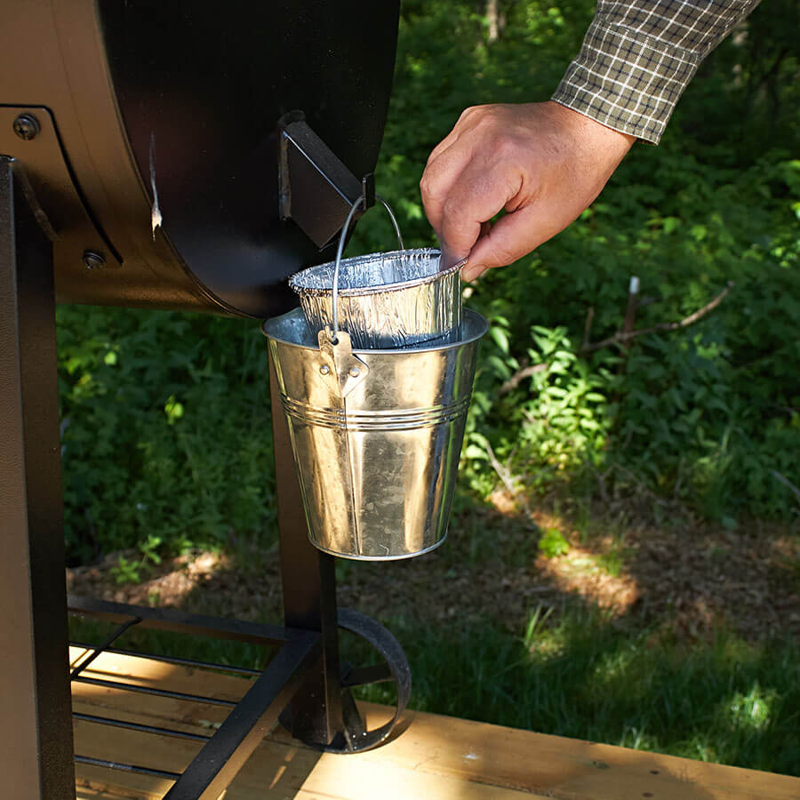 Silver metal bucket with handle, attached to a grill's grease tray.