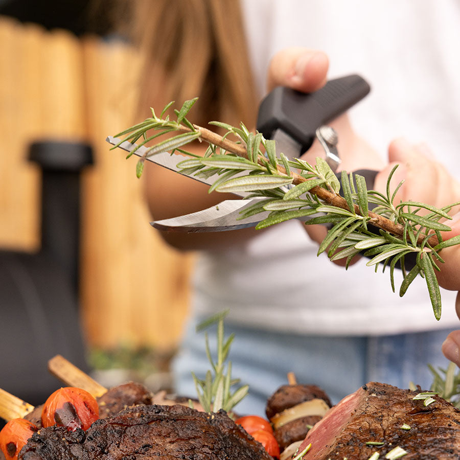 Rosemary sprig being trimmed with a knife, ready for grilling.
