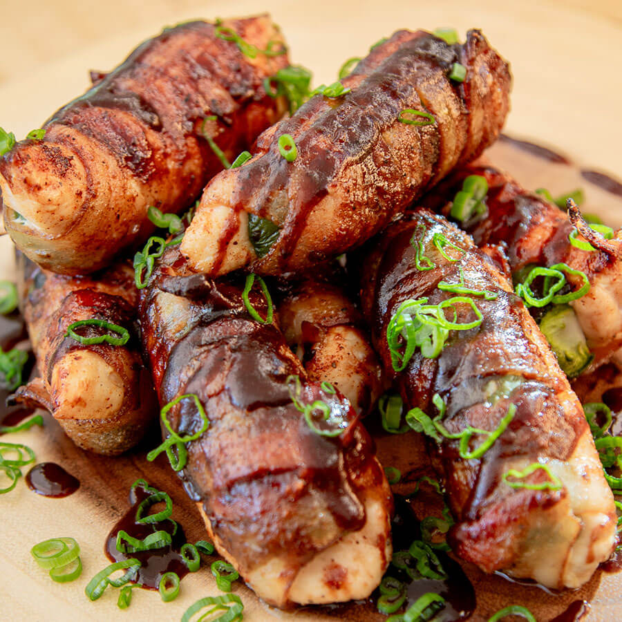 Grilled bacon-wrapped scallops with green onion garnish and sauce.