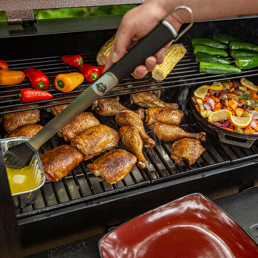 Black grill with chicken, corn, peppers, and vegetables cooking.