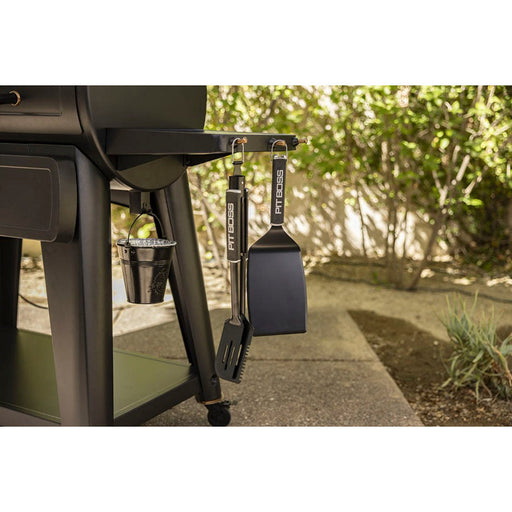Black Pit Boss grill accessories hanging on a barbecue with a bucket below.