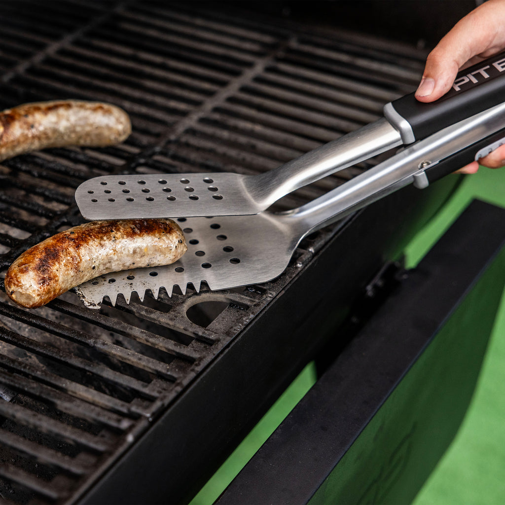 Stainless steel grilling tongs with perforated blades, gripping sausage on a barbecue grill. Ergonomic handle for easy use.
