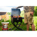 Portable black pellet grill with open lid, grilling meat and vegetables outdoors. Bag of hardwood pellets beside grill.