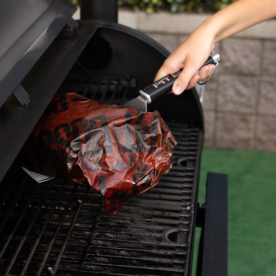 Black Pit Boss tongs lifting a wrapped meat package from a grill.