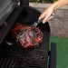 Black Pit Boss tongs lifting a wrapped meat package from a grill.
