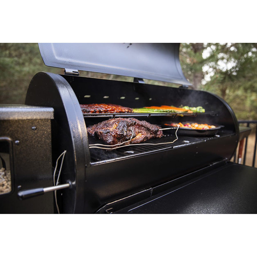 Black pellet grill with open lid, cooking meat and vegetables.