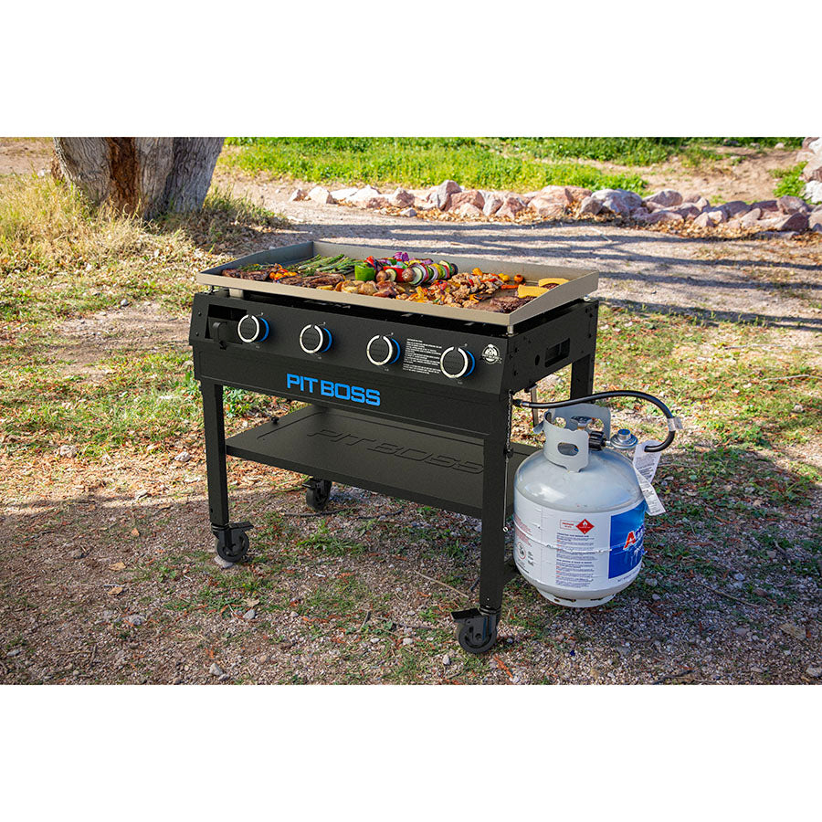 Black Pit Boss outdoor grill with propane tank, cooking vegetables and meat.