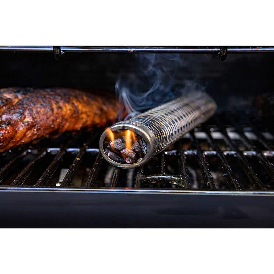 Stainless steel smoker tube with wood pellets, producing smoke on a grill for enhanced BBQ flavor.