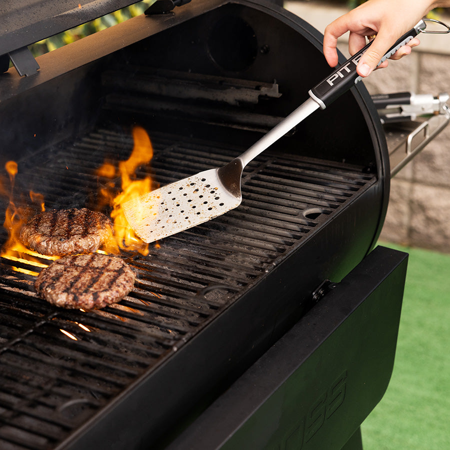 Black Pit Boss grill with spatula flipping burgers over flames.