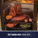 "Black smoker with 1077-square-inch cooking space, featuring meats, sausages, and vegetables."