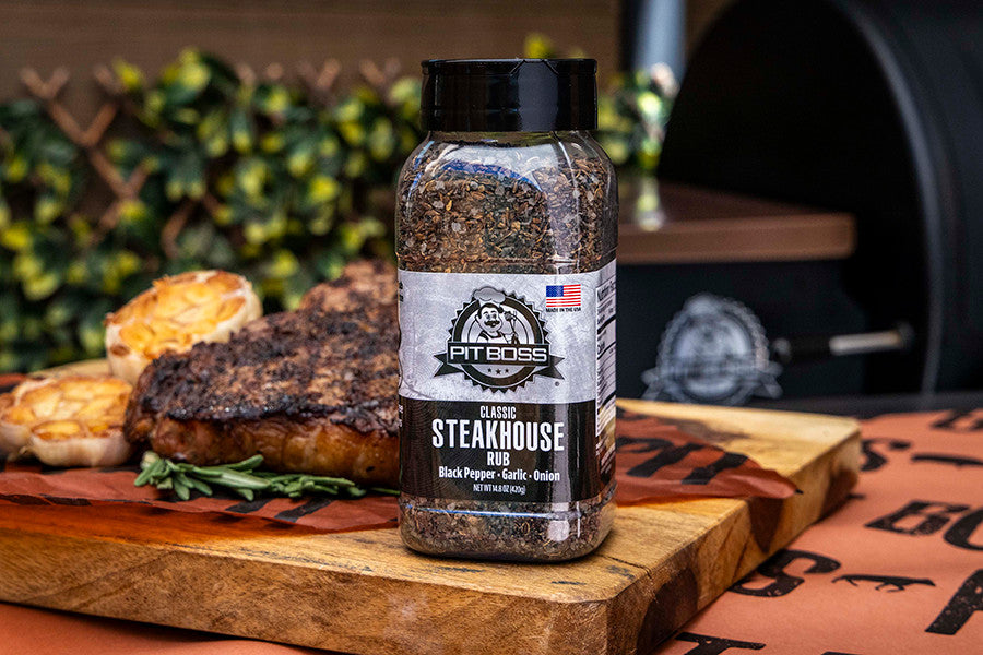 Black Pit Boss Classic Steakhouse Rub spice blend on wooden cutting board with grilled steak and roasted garlic.