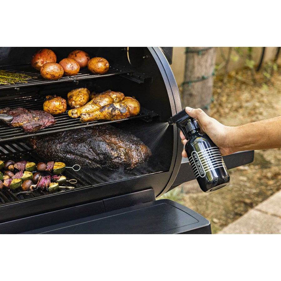 Black spray bottle being used to clean a multi-level grill with food cooking.