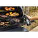 Black spray bottle being used to clean a multi-level grill with food cooking.