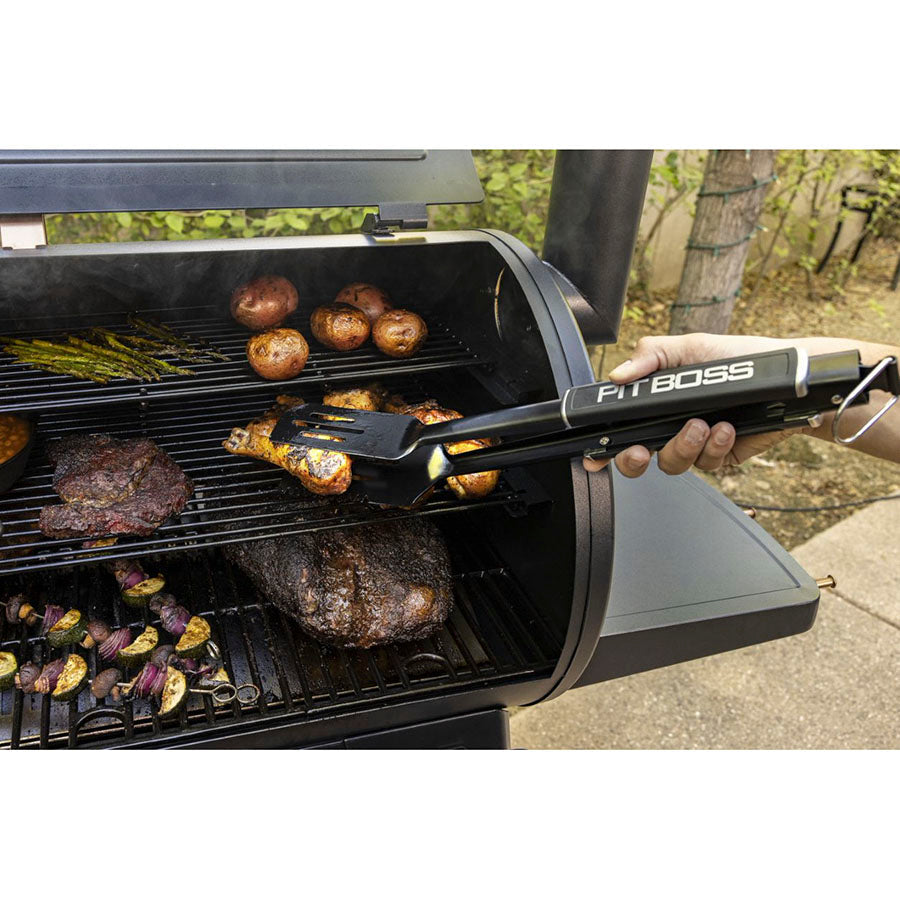 Black FitBoss grill spatula in use on a black outdoor grill with food cooking.