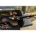 Black FitBoss grill spatula in use on a black outdoor grill with food cooking.