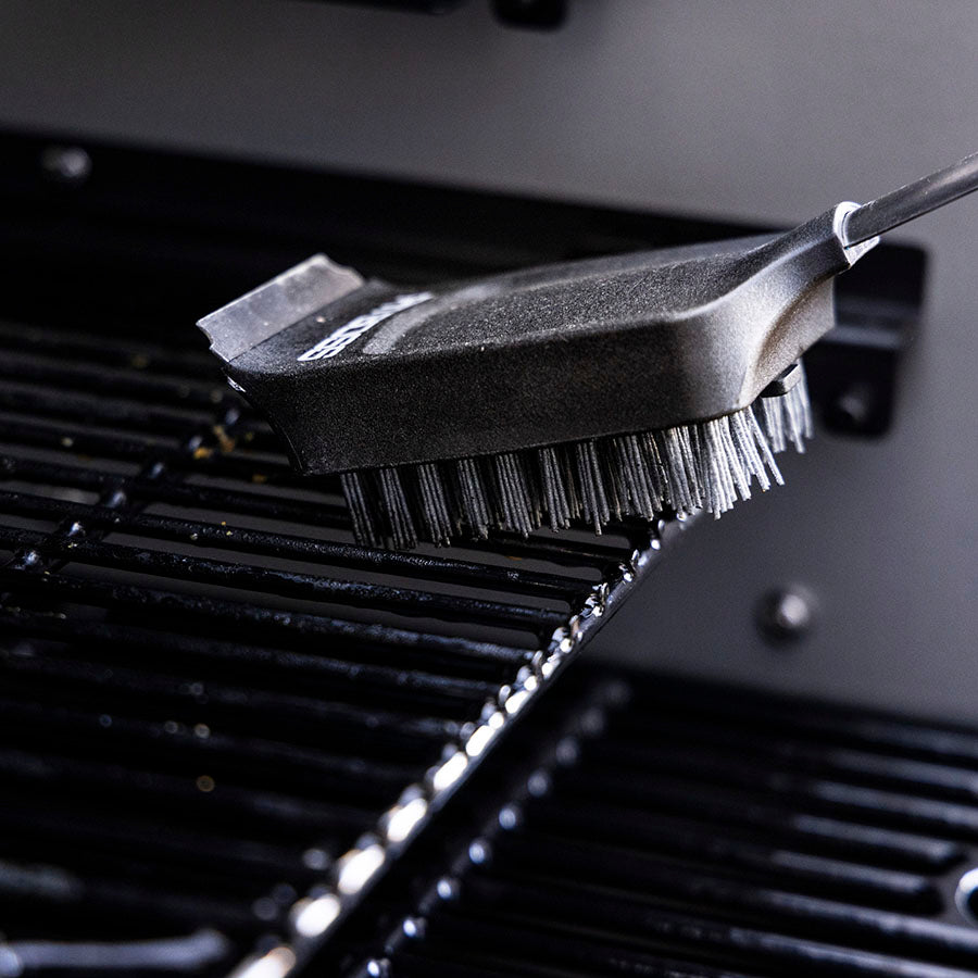 Black grill brush with metal bristles cleaning a grill surface.