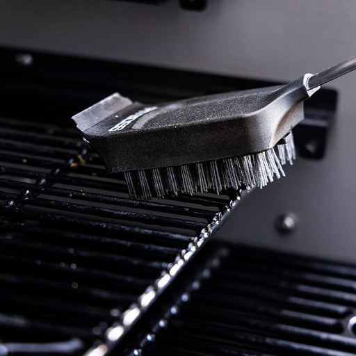Black grill brush with metal bristles cleaning a grill surface.