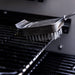 Black grill brush with metal bristles cleaning a grill surface.