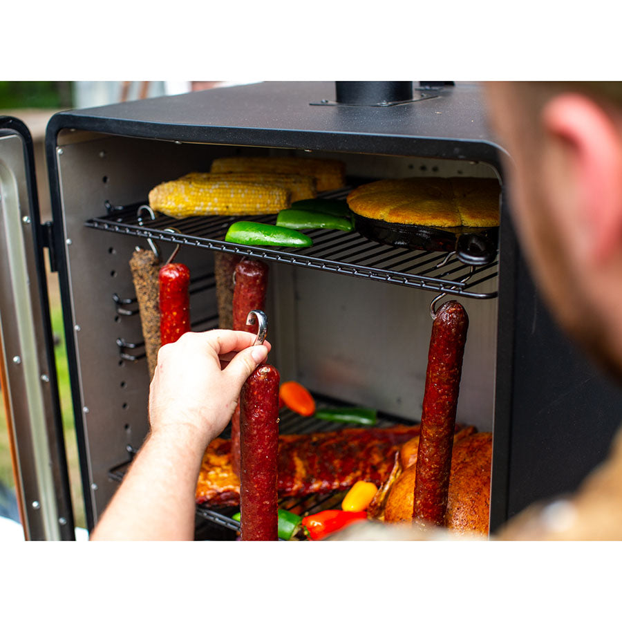 Black electric smoker with various meats and vegetables cooking inside.