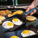 Black Pit Boss spatula lifting fried eggs on griddle.