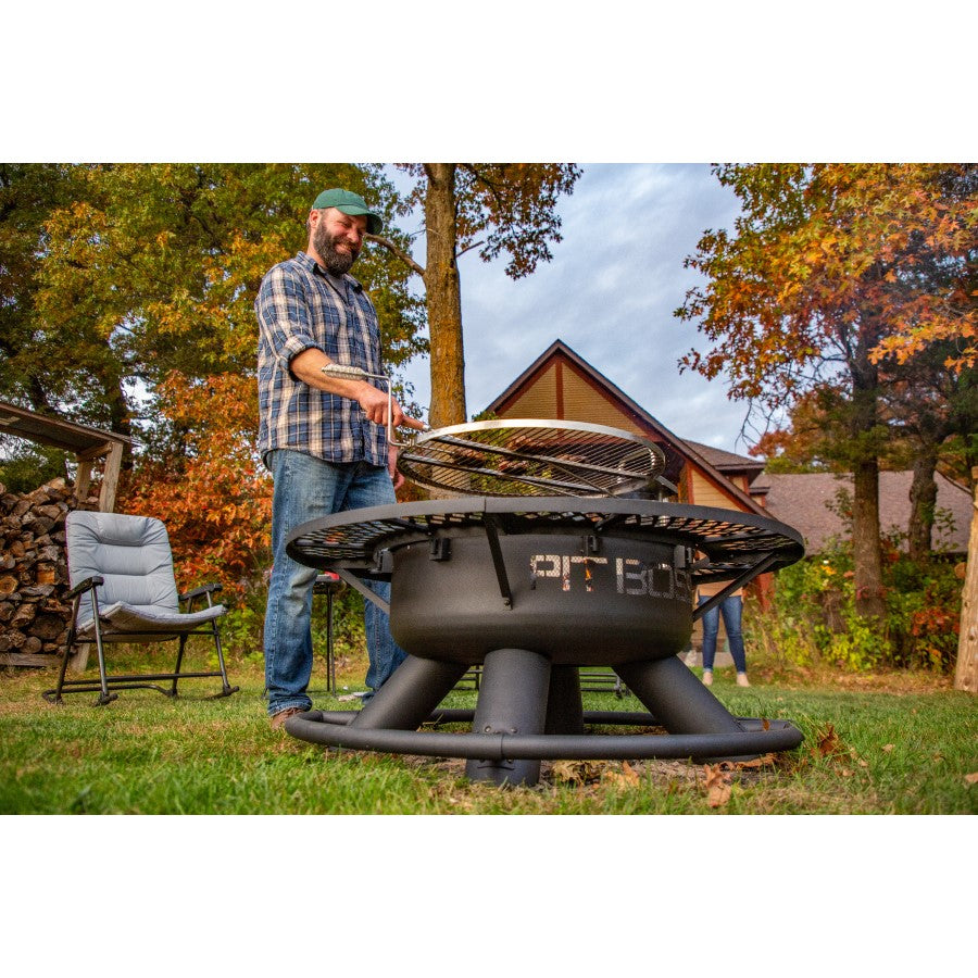 Outdoor fire pit with grill, black metal, round base, used for cooking in a backyard setting.