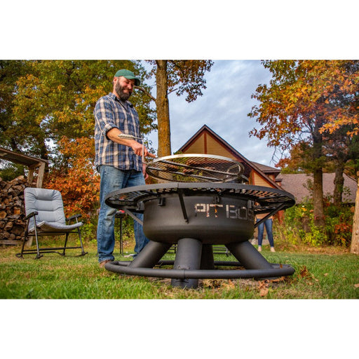 Outdoor fire pit with grill, black metal, round base, used for cooking in a backyard setting.