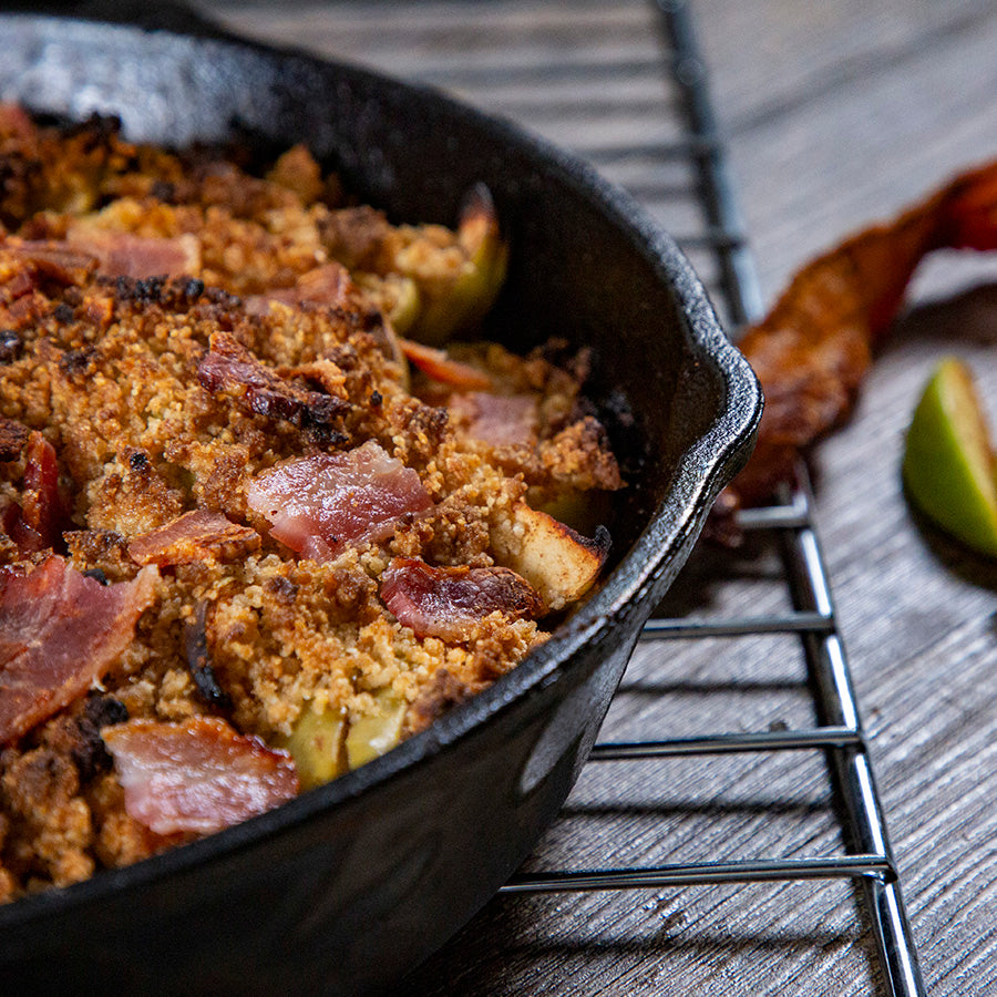 Black cast iron skillet with apple crumble topped with bacon and crumbly topping.