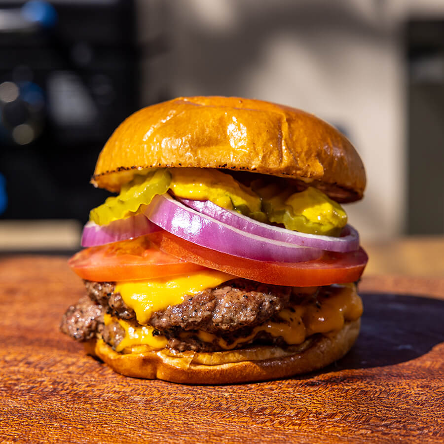 Golden-brown burger with melted cheese, tomato, onion, and pickles on a bun.