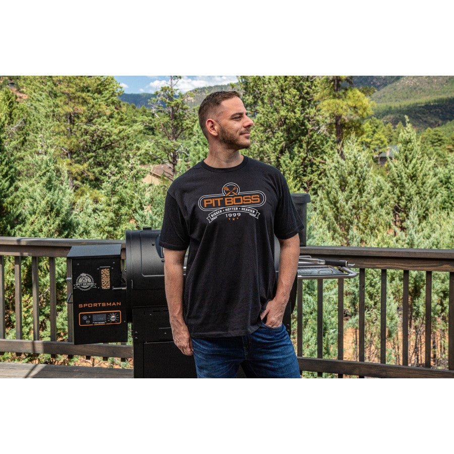 Black Pit Boss t-shirt with "Bigger, Hotter, Heavier" slogan, worn by a man outdoors.