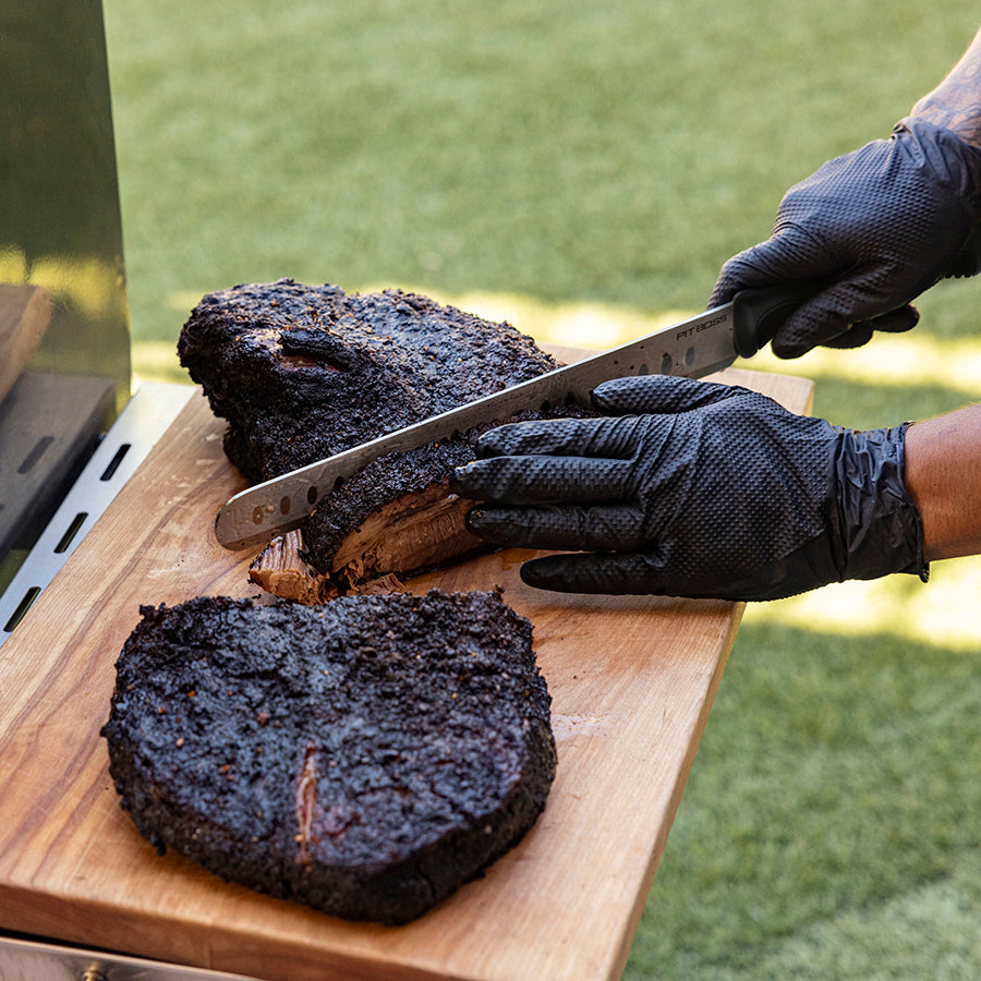 Black-handled knife slicing smoked brisket on wooden cutting board.