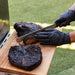 Black-handled knife slicing smoked brisket on wooden cutting board.