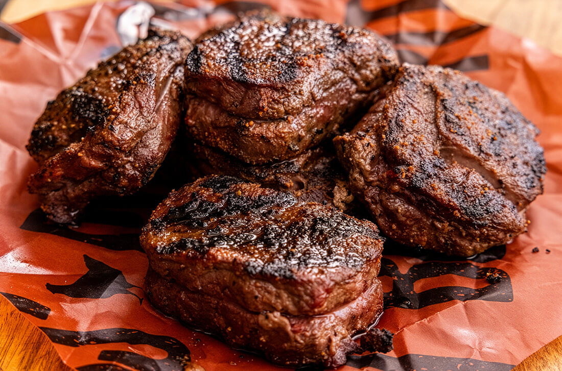 Grilled elk ribeye steaks cooked on Pit Boss wood pellet grill smoker and served on butcher paper with parsley garnish